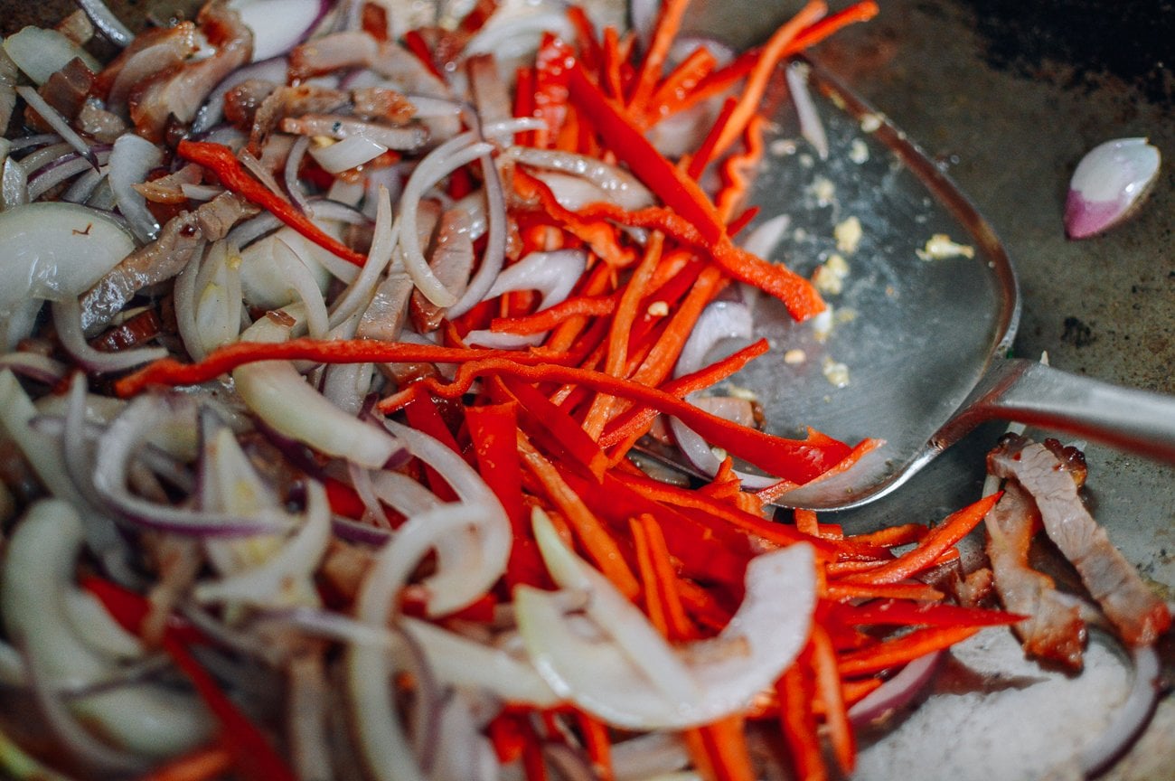 Adding julienned red peppers to onions and char siu