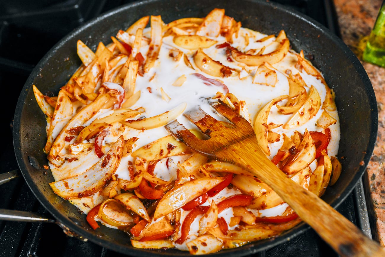 adding coconut milk to onions and red peppers in red curry paste