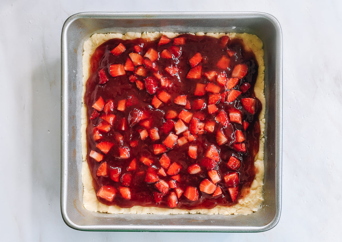 diced strawberries scattered on top of dough with strawberry jam